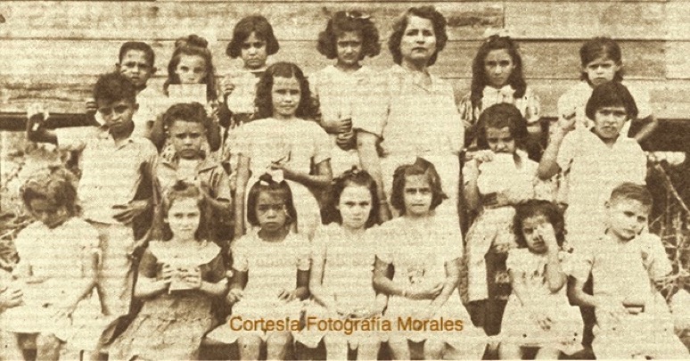 Estudiantes de Primer Grado del Barrio París con la Maestra Antonia Irizarry de Díaz (primera fila) Rita Rivera, Cuchi Pabón, Eddie Blanco, Luisa Rodríguez, Virgenmina Rivera, Nereida Blanco, Efraín Sanoguet; (segunda fila) Pito Morales, Divina Flores, (tercera fila) Obed Morales, Anita Sanoguet, Irma Barros, Gladys Rivera, Henrique y Monserrate. (circa 1941-42). (Cortesía de Fotografía Morales).